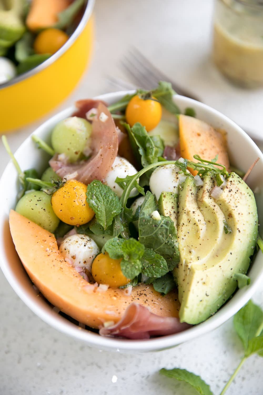 very close up image of bowl filled with melon and mozzarella salad with prosciutto