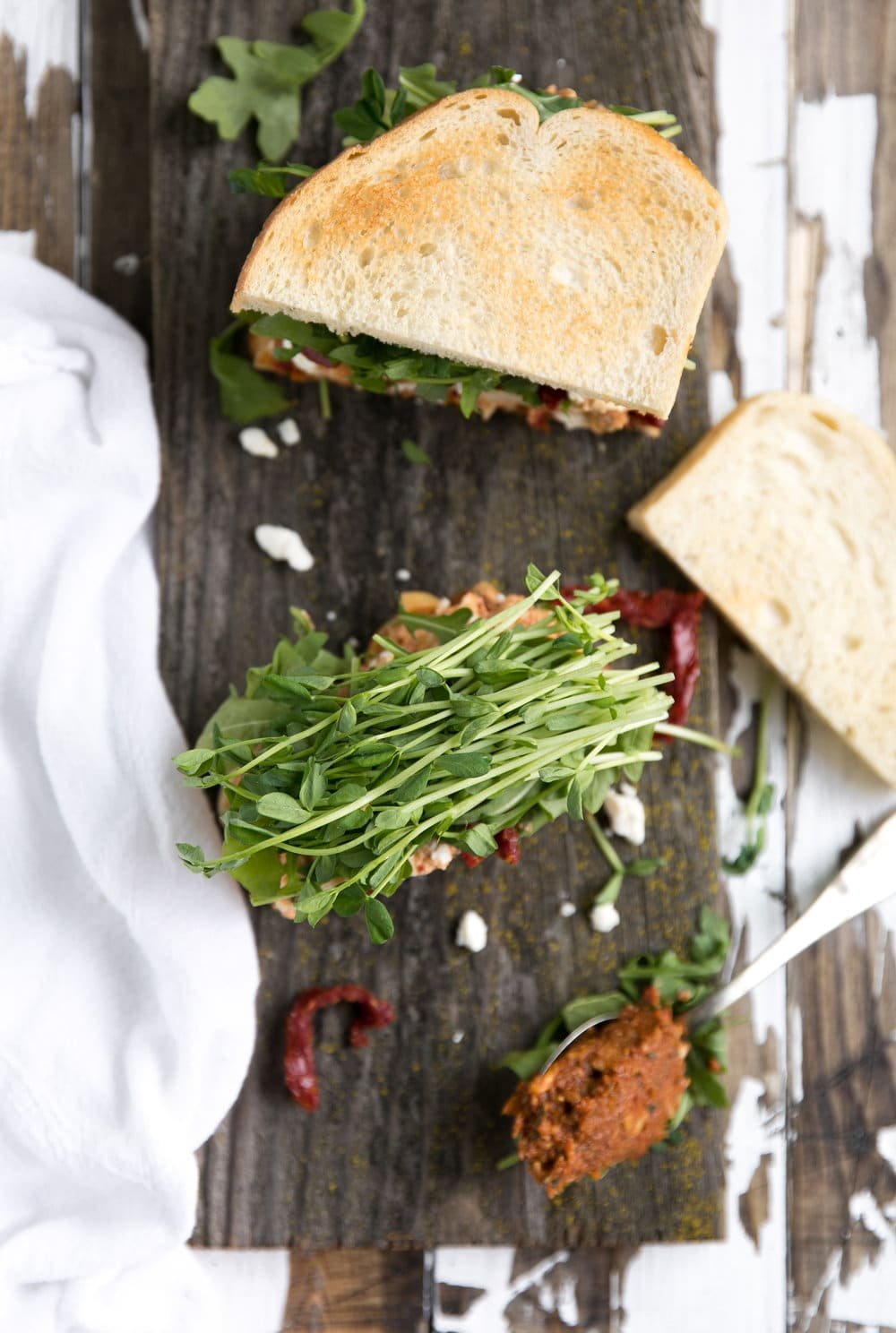 Sun-Dried Tomato Pesto Chicken Salad Sandwich cut in half with greens and pesto sauce