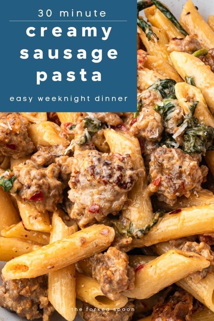 Overhead close-up of creamy sausage pasta with penne, spinach, sun-dried tomatoes, and sausage in a Parmesan cream sauce. Blue text overlay at the top reads “30 minute creamy sausage pasta – easy weeknight dinner.”