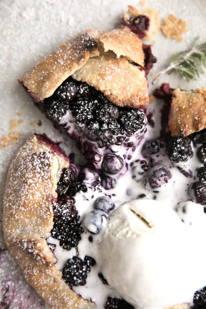One slice cut from a baked blueberry galette topped with melting vanilla ice cream.