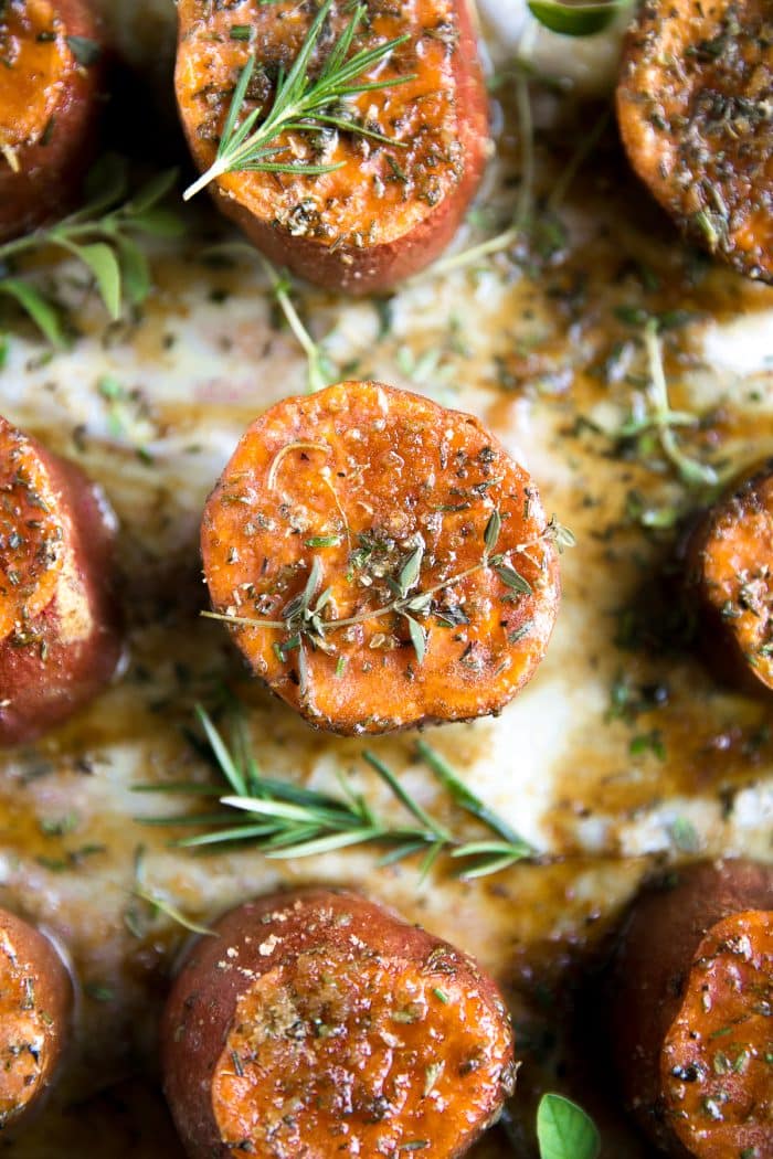 Roasted sweet potatoes on a large baking sheet covered with melted butter, brown sugar, and fresh herbs.