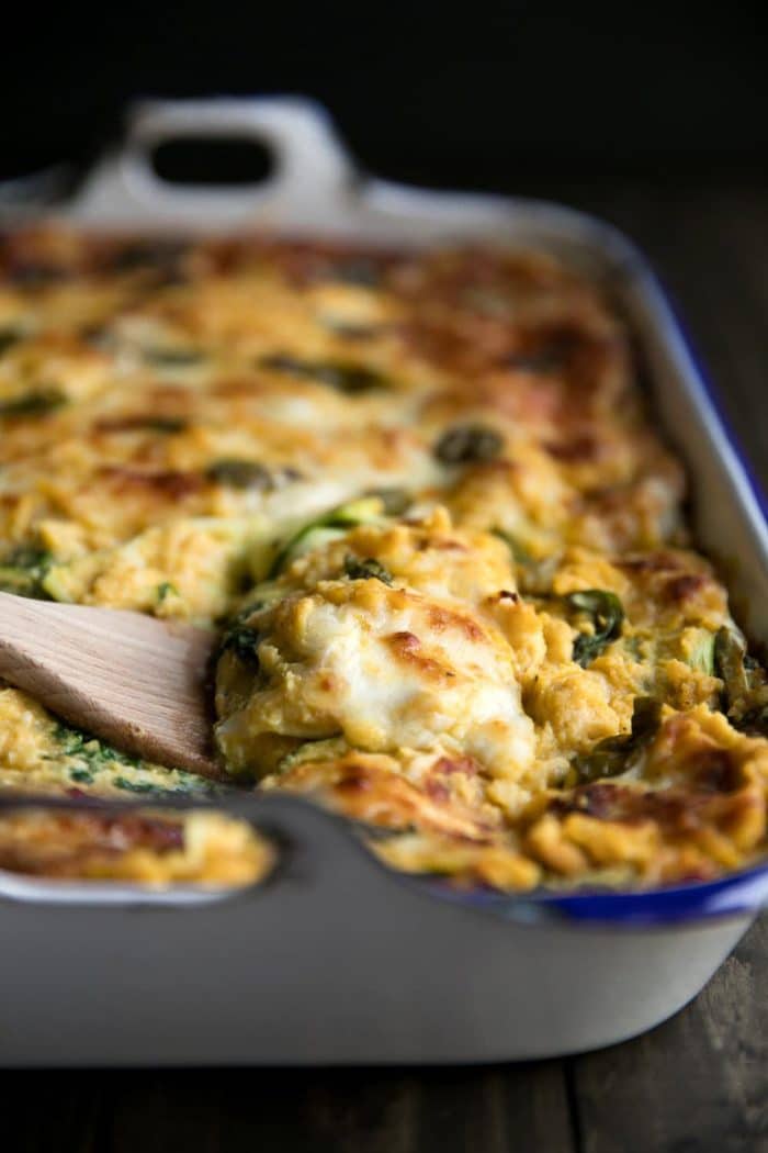 Scooping out a piece of butternut squash lasagna from a large white baking pan.