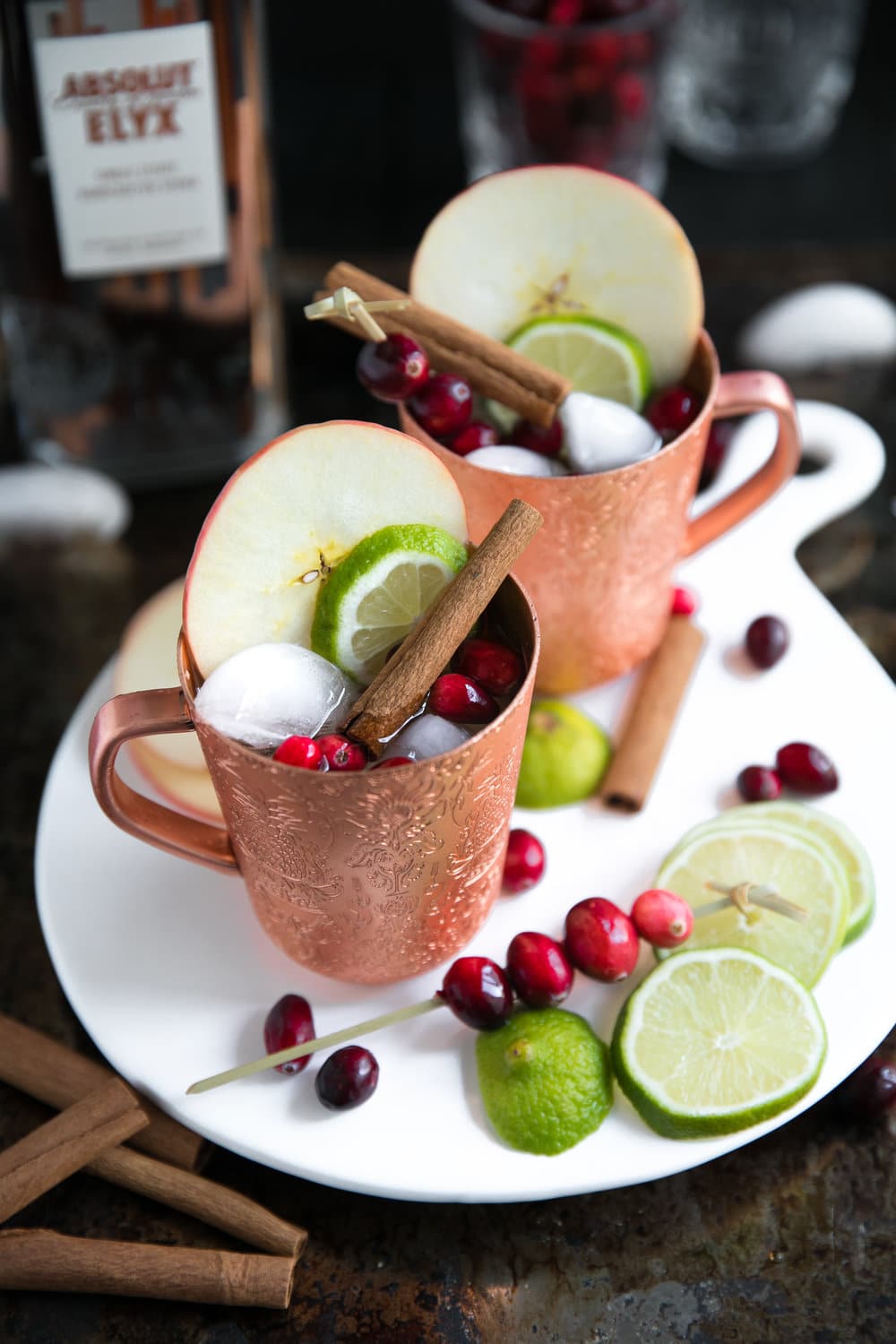 Copper mugs filled Cranberry Apple Cider Moscow Mule garnished with apple and cinnamon sticks