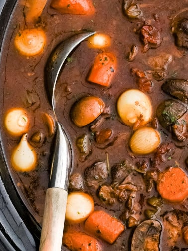 Slow cooker filled with slowly cooked beef bourguignon with carrots, pearl onions, celery, and tender chunks of beef.