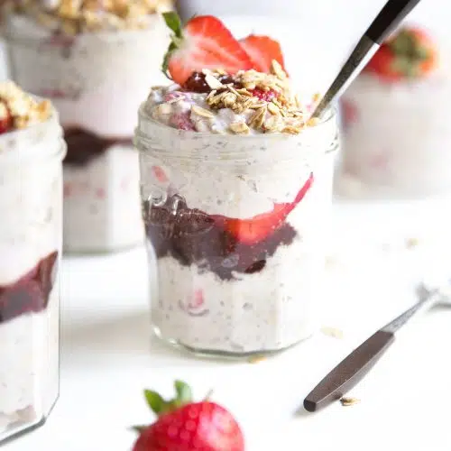 Small jars filled with overnight oats with yogurt and a layer of strawberry jam and fresh strawberries.
