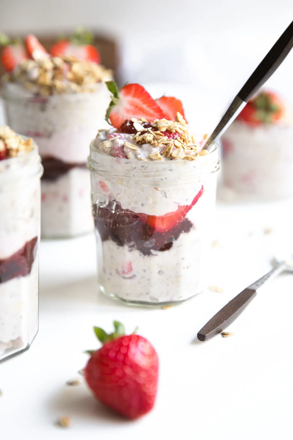 Small jars filled with overnight oats with yogurt and a layer of strawberry jam and fresh strawberries.