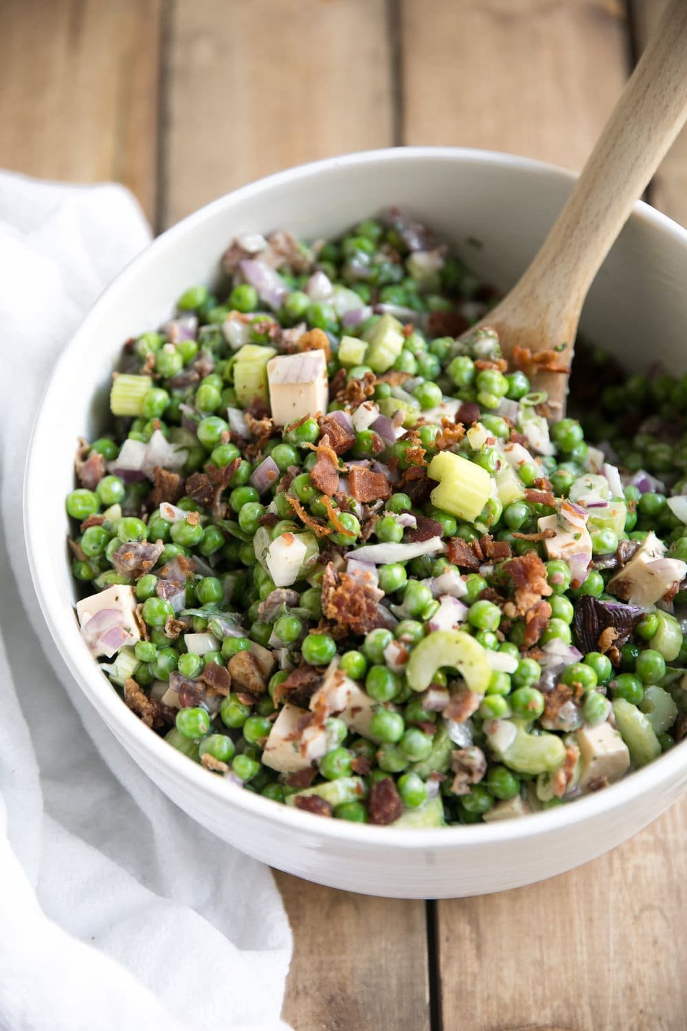 Large salad bowl filled with peas, bacon, celery, green onion, red onion, and cubes of smoked gouda all tossed in a creamy Italian mayo dressing.