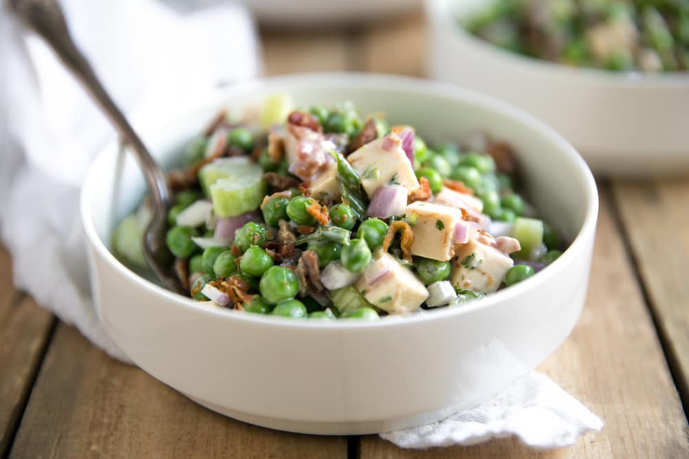 White bowl filled with peas, bacon, celery, green onion, red onion, and cubes of smoked gouda all tossed in a creamy Italian mayo dressing.