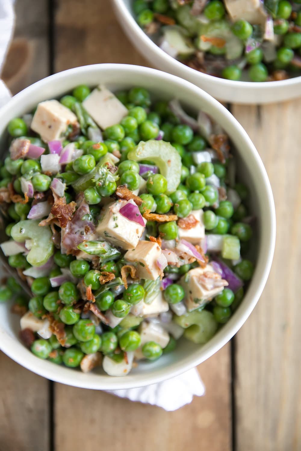 White bowl of pea salad with crispy bacon, celery, gouda, and red onion in a creamy Italian mayo dressing.