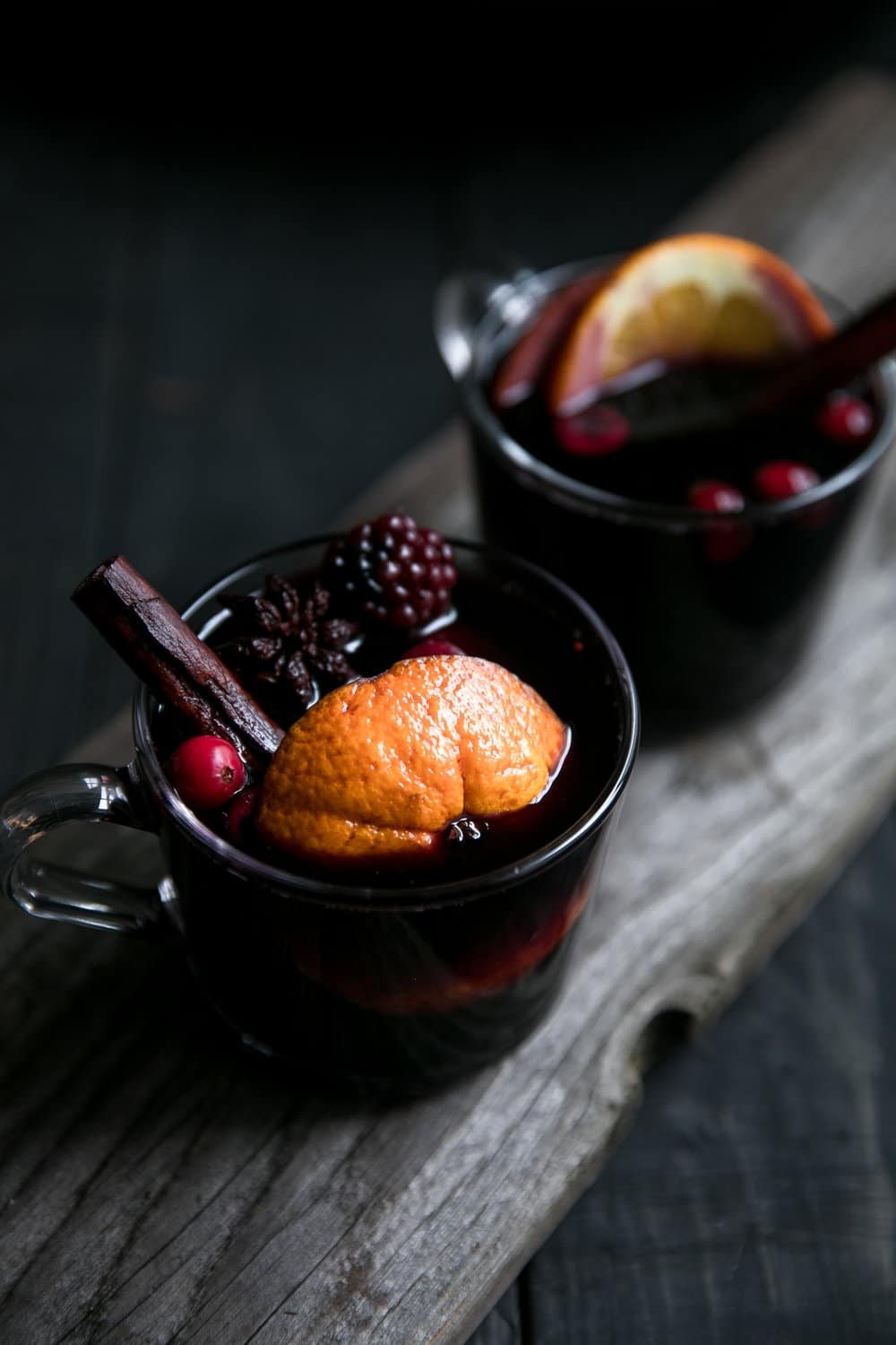 Two clear glasses filled with mulled wine and garnished with orange slices, cinnamon sticks, and blackberries.