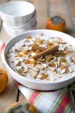 Large white bowl filled with creamy rice pudding topped with raisins, almonds, and cinnamon.