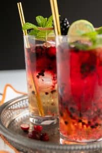 Two highball glasses filled with ginger beer, vodka, and fresh blackberries and raspberries.