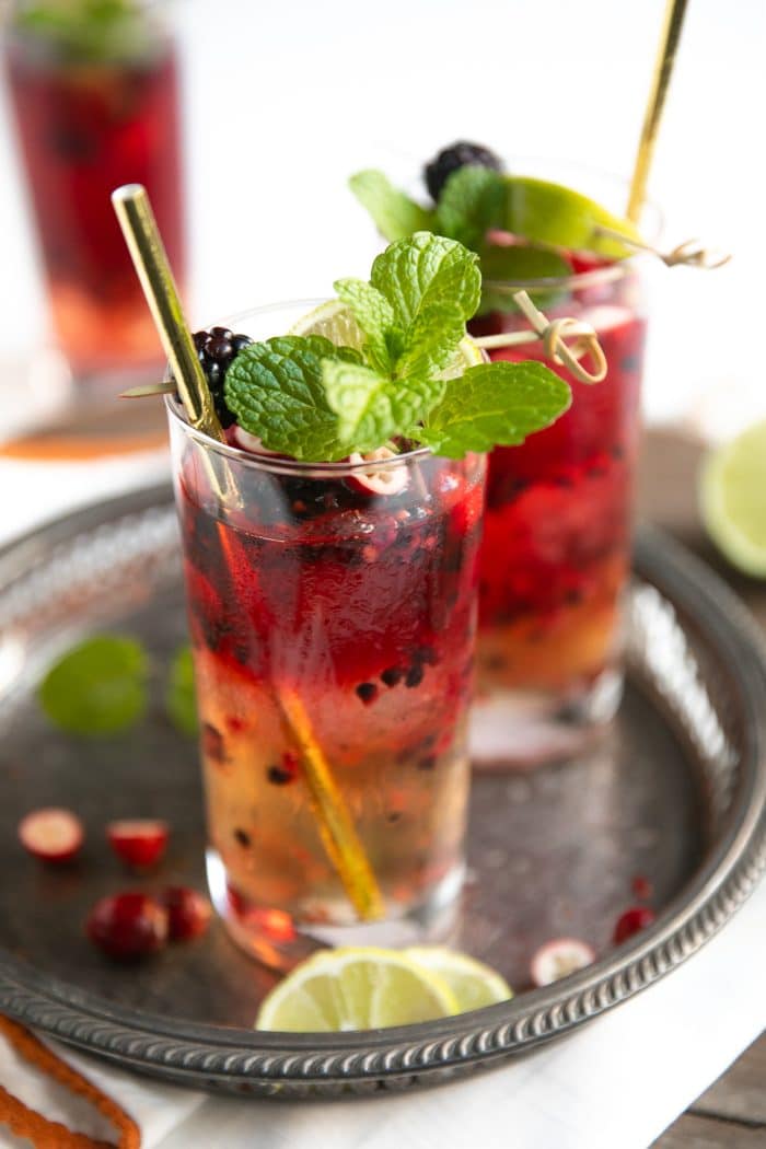 Two highball glasses filled with ginger beer, vodka, and fresh blackberries and raspberries.