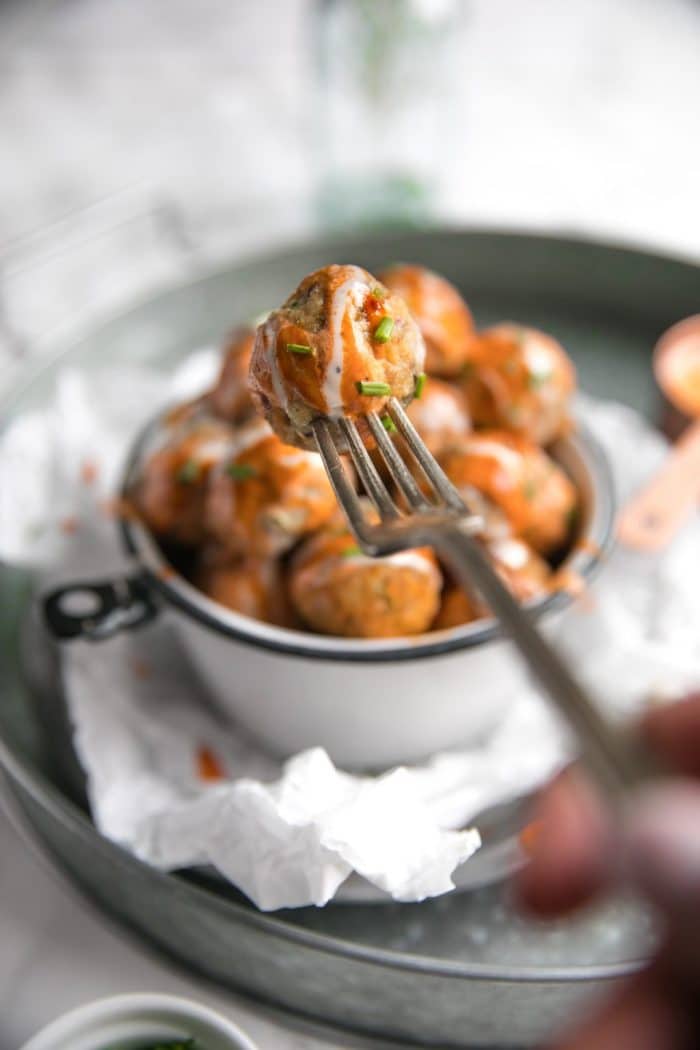 Fork holding one buffalo meatball with remaining meatballs blurred in the background