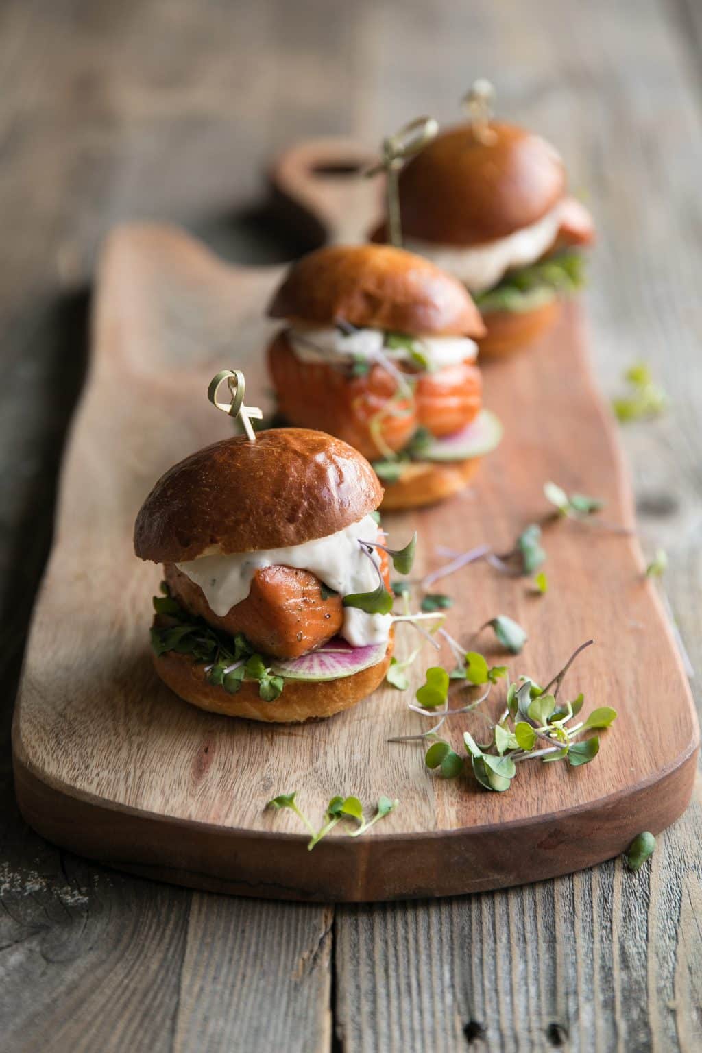 Three Grilled Salmon Sliders with Garlic Lemon Aioli on a wood serving board.