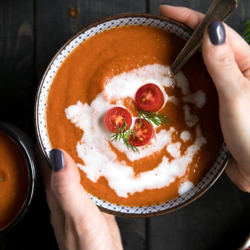 A person holding a bowl of food, with Roasted Red Pepper Soup and Tomato