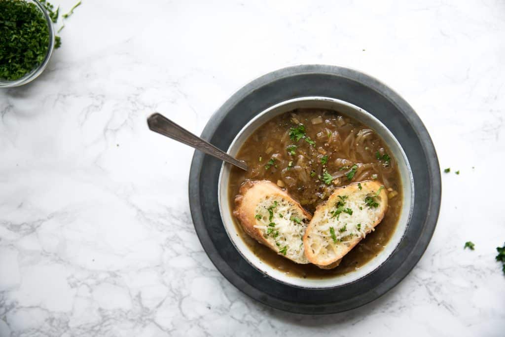 Bowl filled with homemade onion soup made with caramelized onions and topped with crispy parmesan toasts.