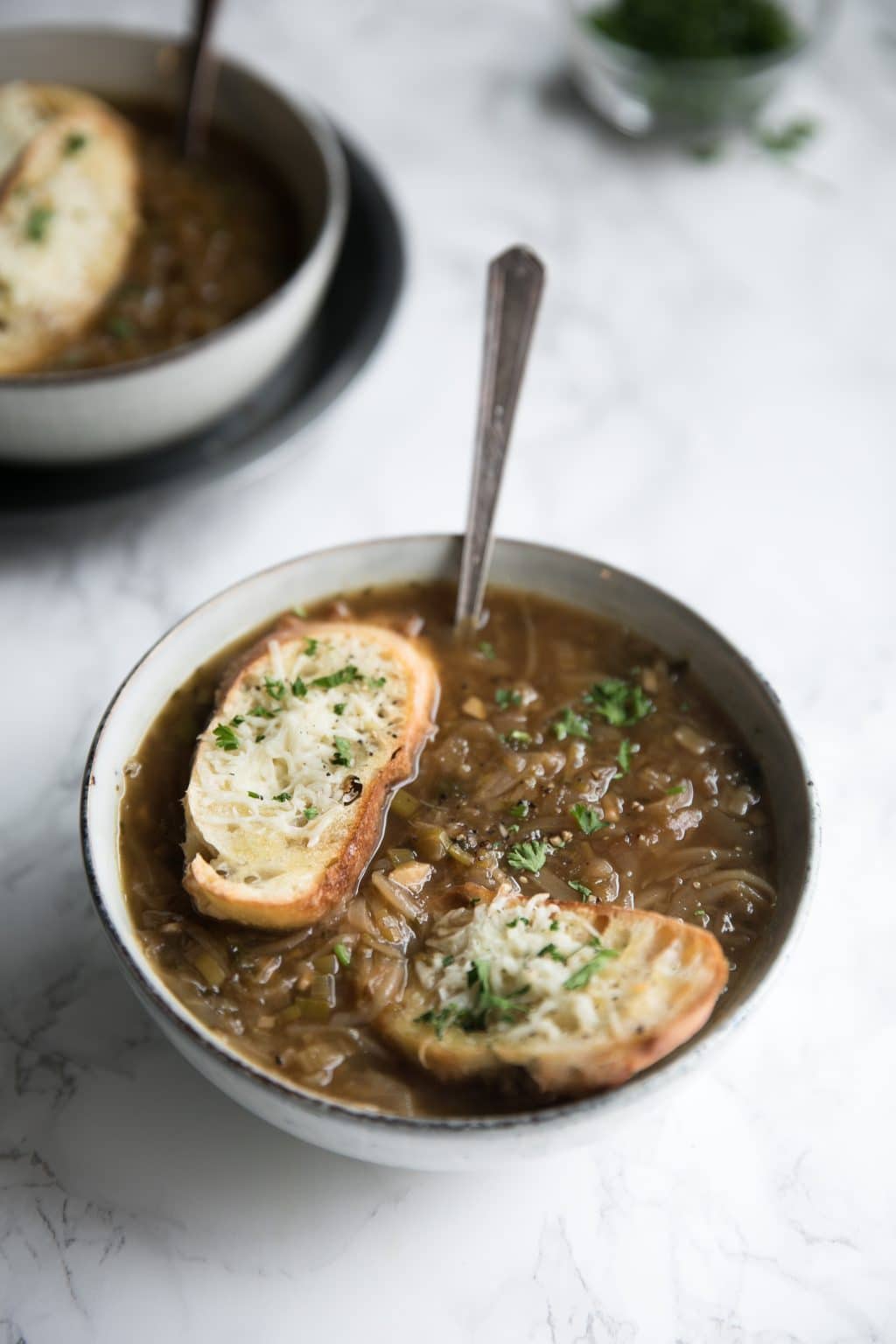 Bowl filled with homemade onion soup made with caramelized onions and topped with crispy parmesan toasts.