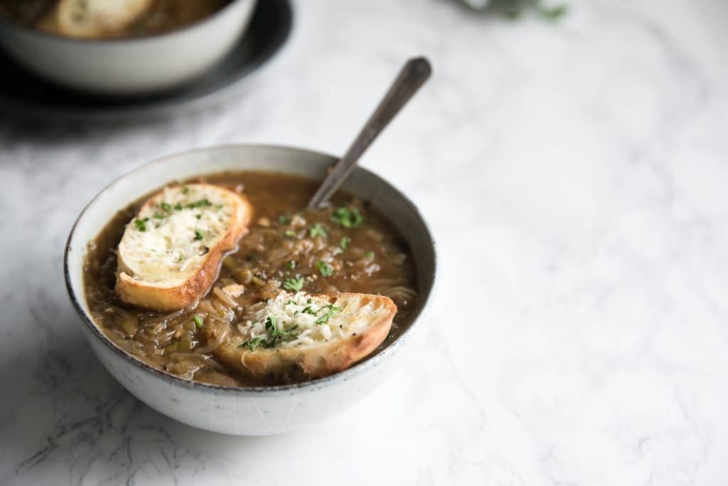 Bowl filled with homemade onion soup made with caramelized onions and topped with crispy parmesan toasts.