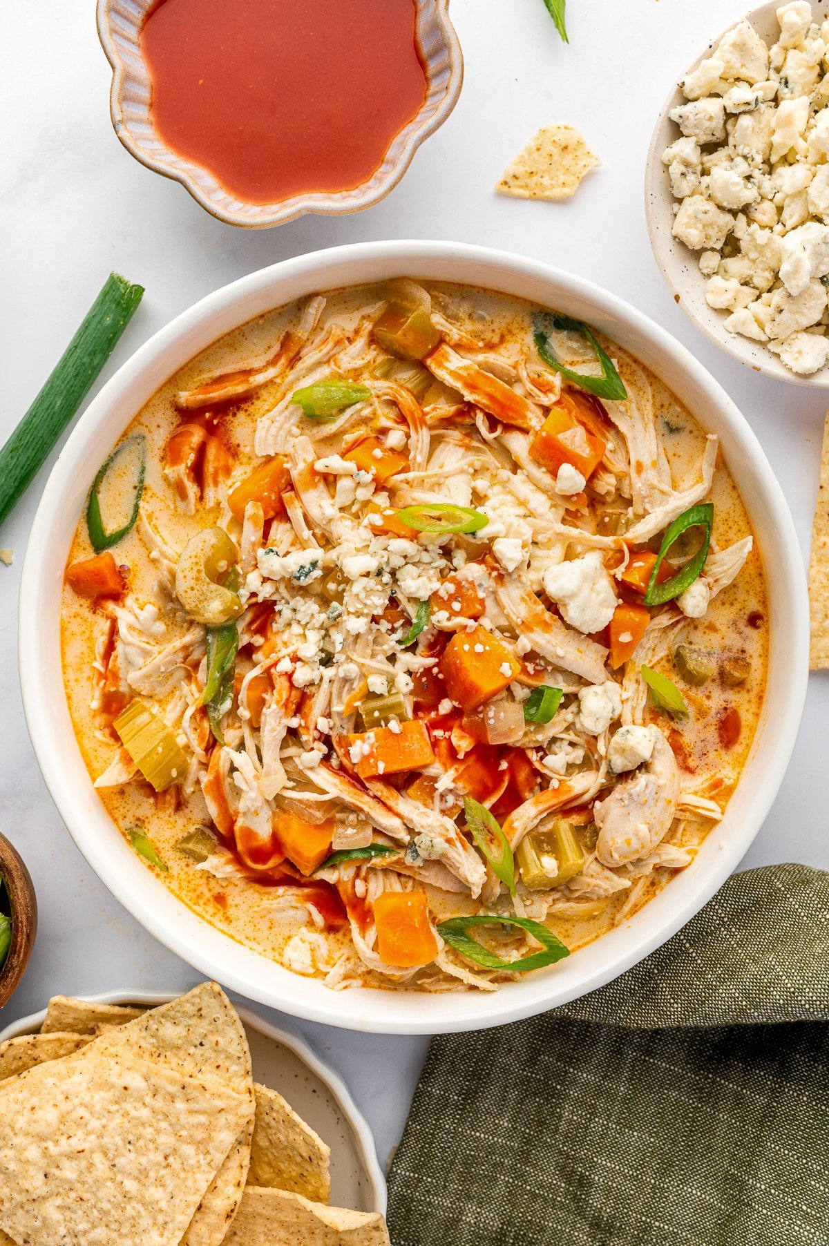 Overhead view of a bowl filled with creamy buffalo chicken soup, topped with green onions and blue cheese.