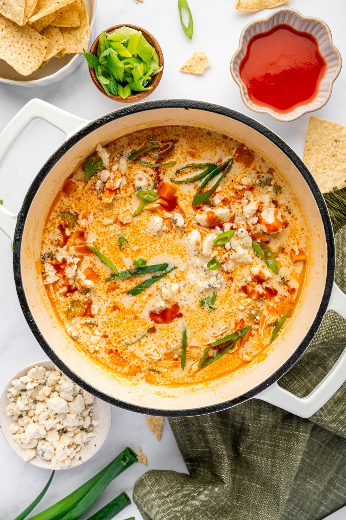 A white pot filled with creamy buffalo chicken soup topped with green onions and blue cheese