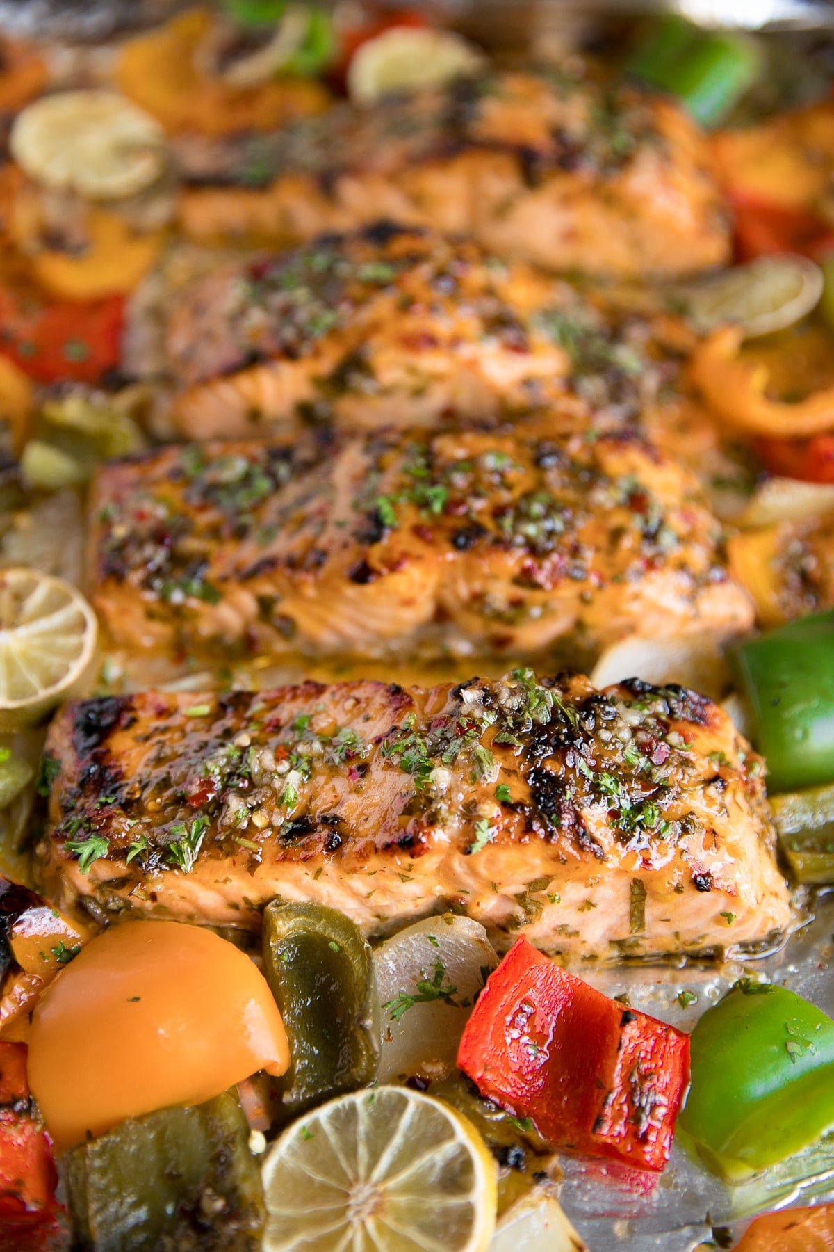 Large baking sheet with four salmon fillets baked in a marinade of orange juice and lime juice and sweet chili sauce with muli-colored bell peppers and onions..