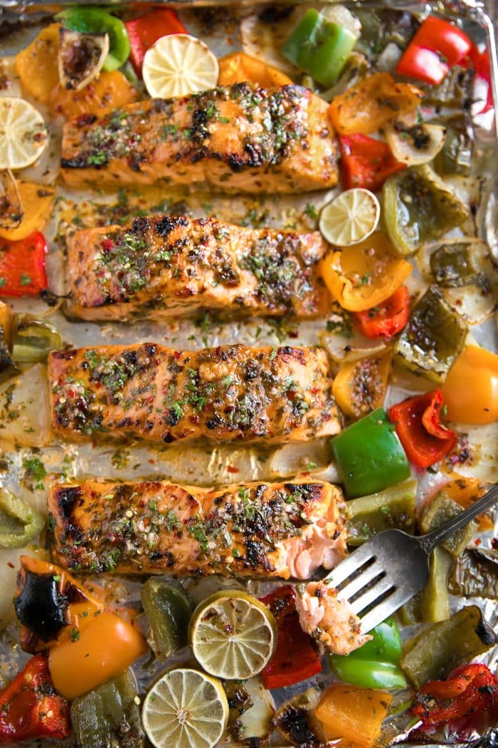 Large baking sheet with four salmon fillets baked in a marinade of orange juice and lime juice and sweet chili sauce with muli-colored bell peppers and onions..