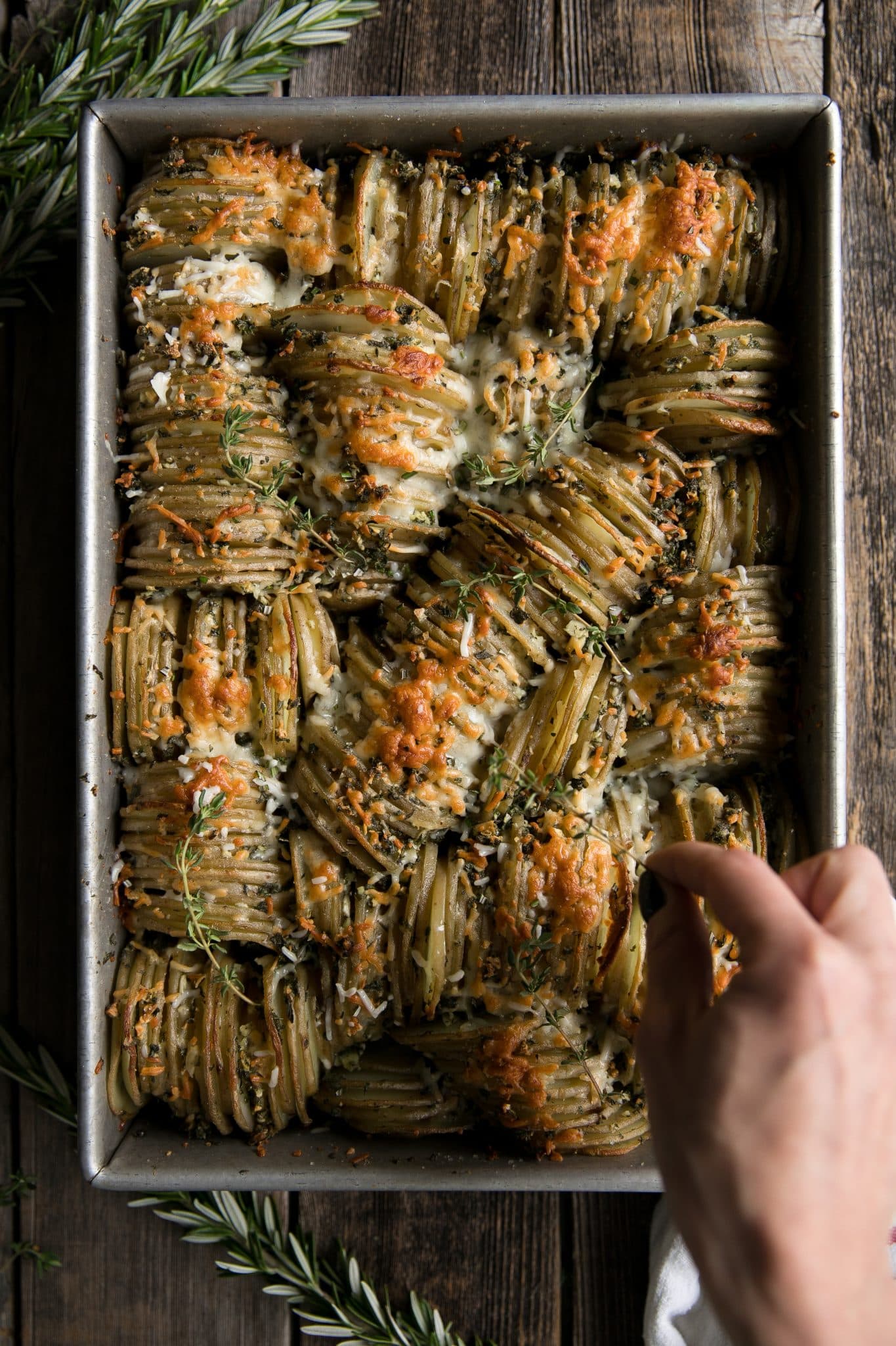 Adding final garnishes to a baking dish filled with crispy hasselback potato casserole.