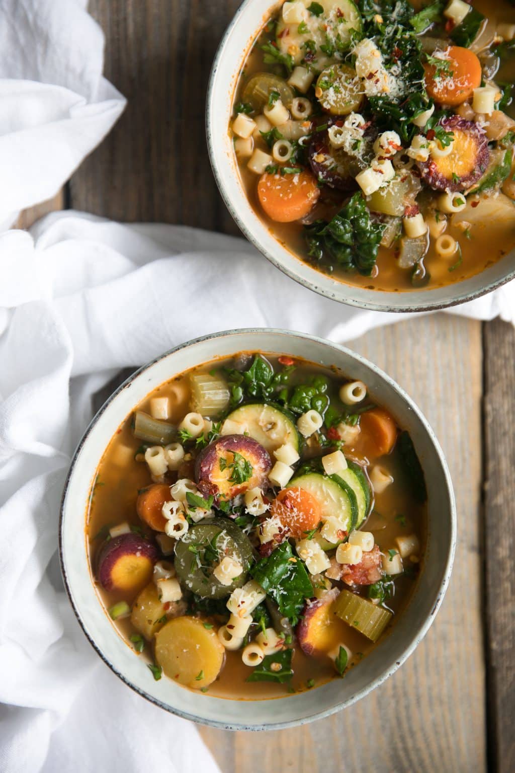 Two bowls filled with Minestrone soup made with mixed seasonal vegetables and pasta noodles.