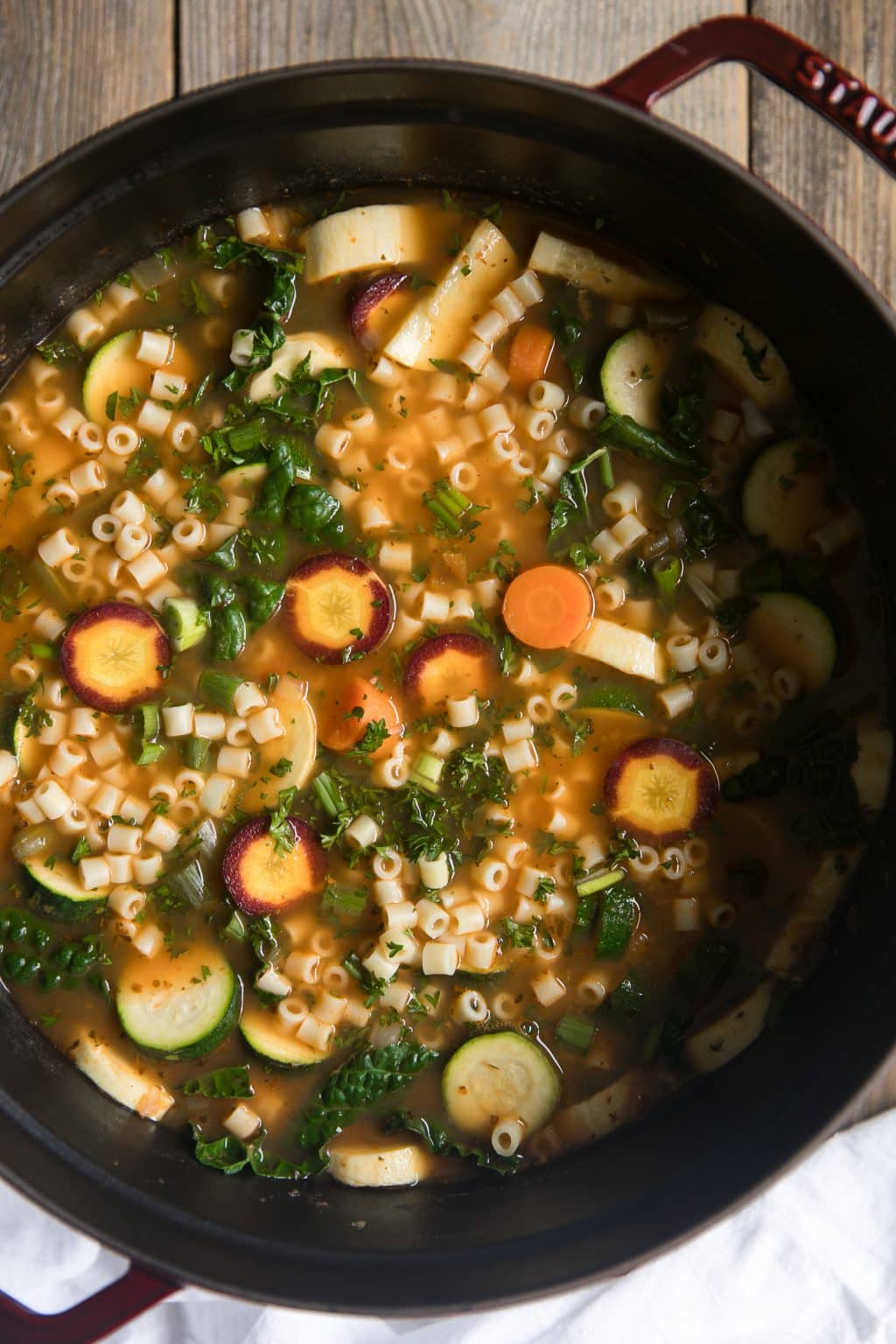 Large cast iron pot filled with carrots, kale, pasta, zucchini, squash in a tomato broth.