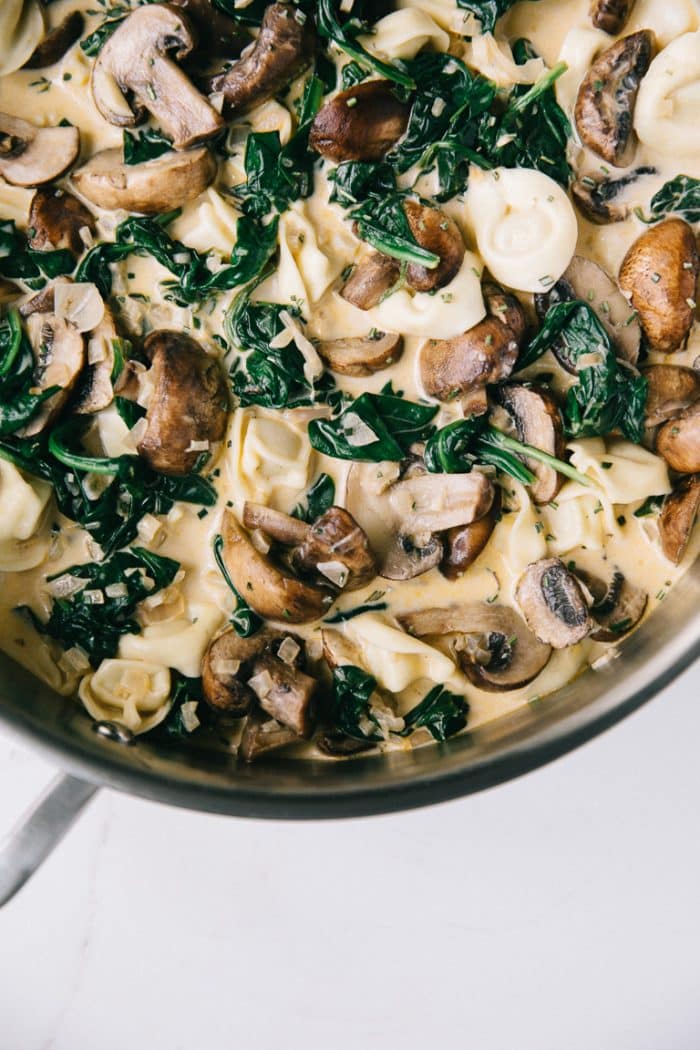 Metal Pot filled with Cheese tortellini, mushrooms, and spinach in a rich cream sauce.
