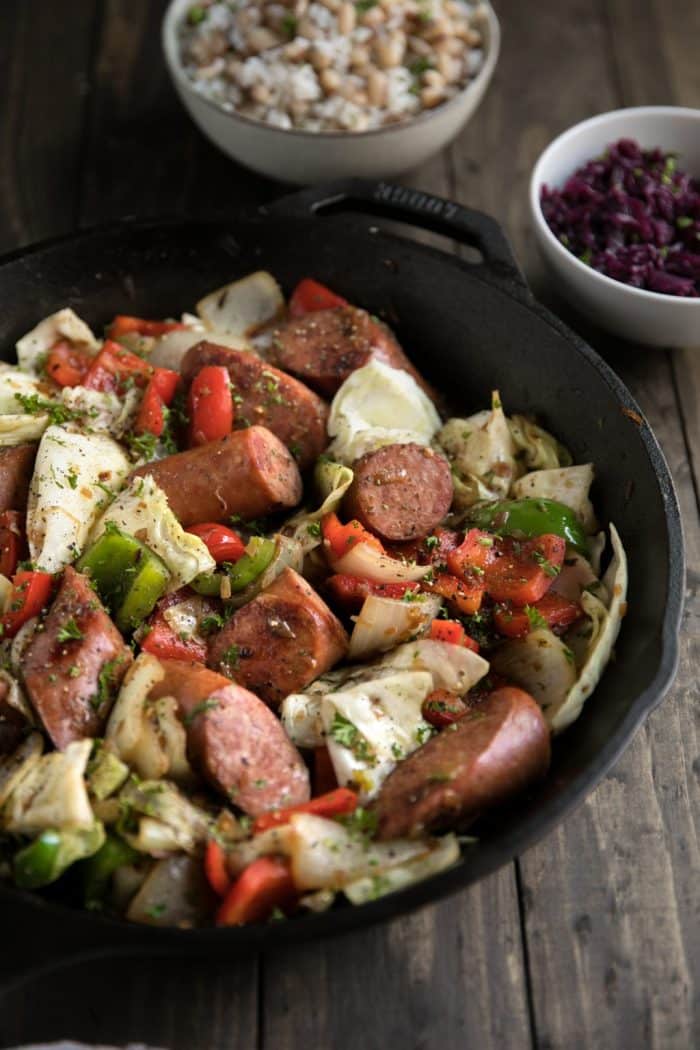 Black skillet with cooked onions, cabbage, kielbasa, and bell peppers.