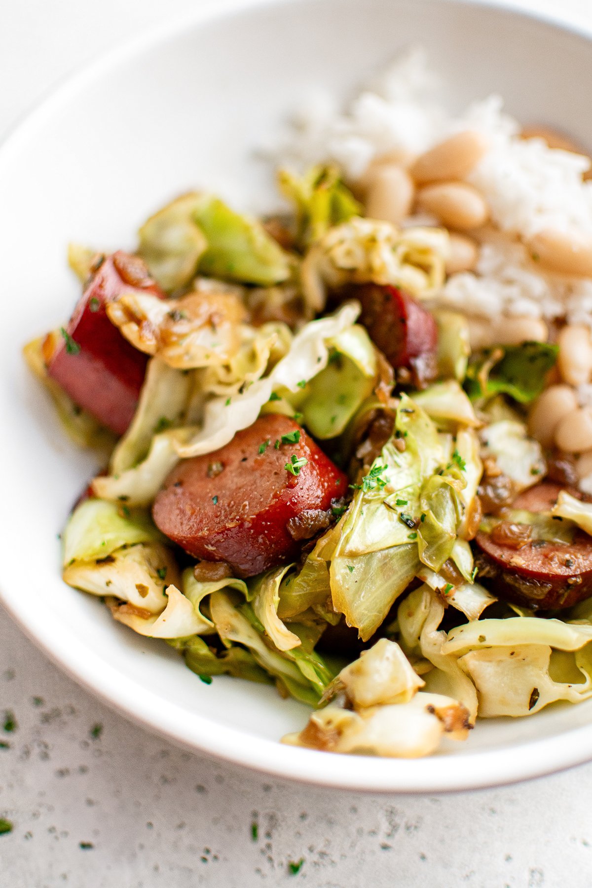 Close-up of kielbasa and cabbage served in a white bowl with rice and beans.