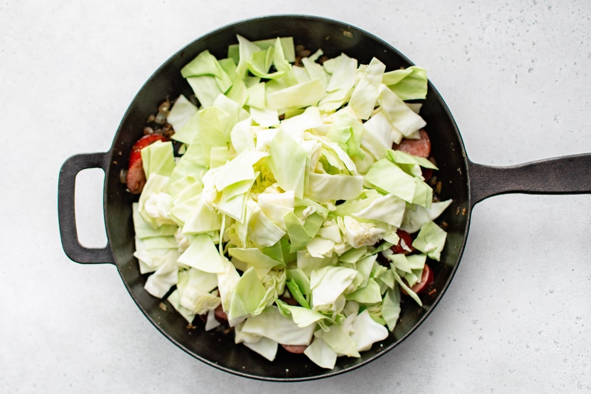 Fresh chopped cabbage added on top of browned kielbasa and onions in a skillet.