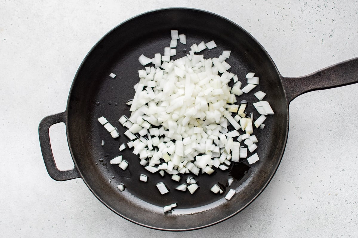Chopped yellow onion cooking in olive oil in a large black skillet.
