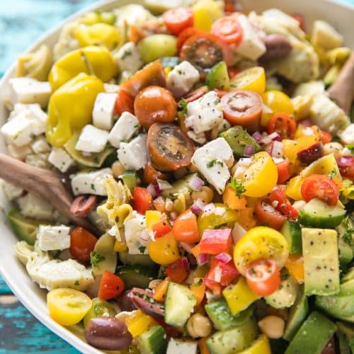 Large white bowl filled with chopped Mediterranean salad made with fresh veggies, artichoke hearts, avocado, chickpeas, feta cheese.