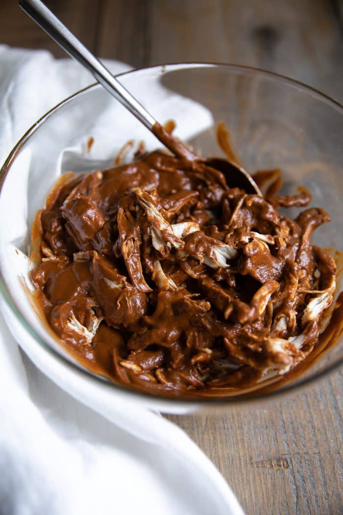 Glass bowl filled with mole sauce and shredded chicken.