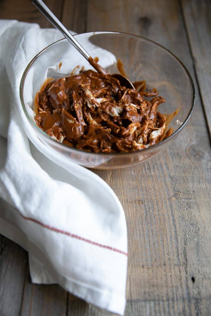 Glass bowl filled with mole sauce and shredded chicken.