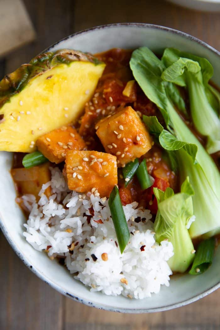 Bowl filled with a rich coconut Thai fish curry with rice, pineapple wedges, and baby bok choy.