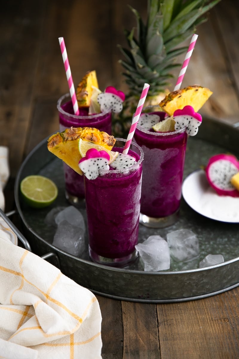 Frozen Pineapple Dragon Fruit Margaritas. Cold, crisp, and refreshing, these Frozen Pineapple Dragon Fruit Margaritas are the perfect solution for all those hot summer days and backyard BBQs. Swap the tequila for pineapple juice to make a healthy, fruit packed smoothie loved by both kids and adults! via @theforkedspoon #margarita #tequila #cocktail #frozenmargarita #drinkrecipe #dragonfruit | https://theforkedspoon.com/ three blended frozen dragon fruit tequila margaritas