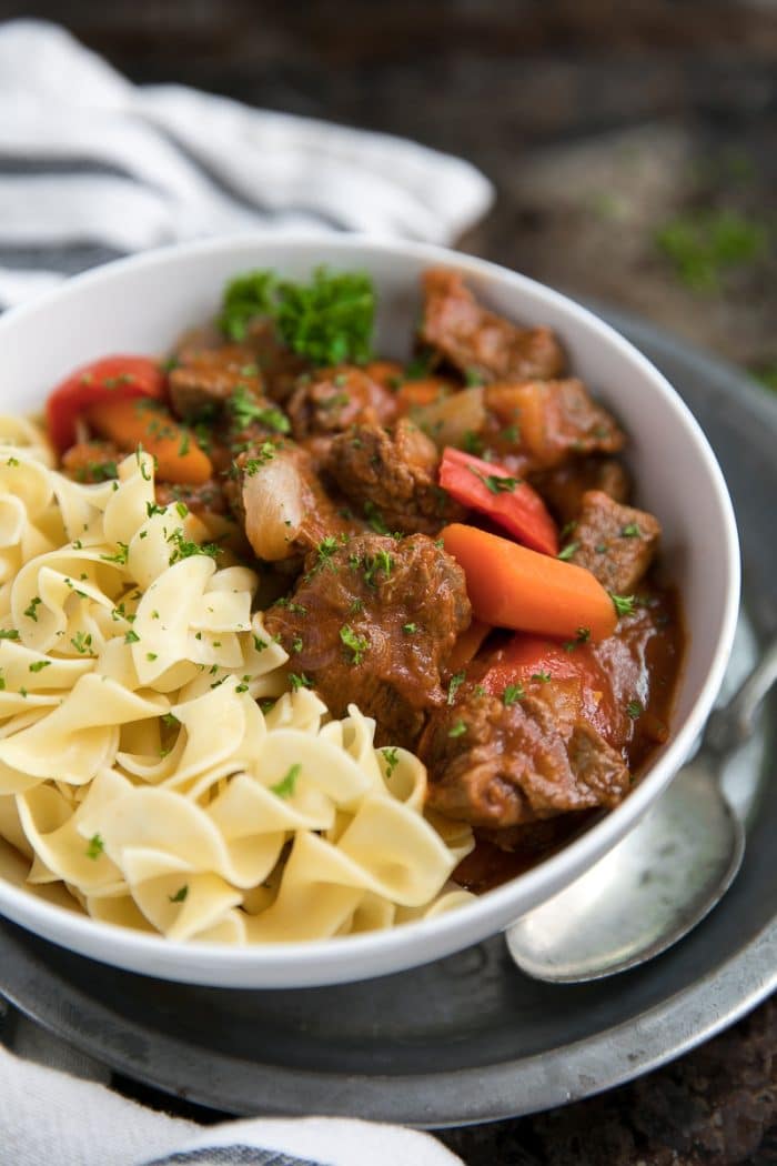 Close-up image of Hungarian beef goulash with egg noodles, bell pepper, and carrots garnished with parsley.