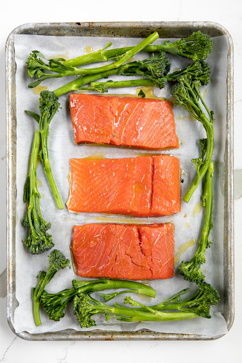 3 salmon filets on a sheetpan with parchment paper and broccolini