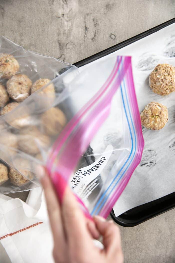 Transferring frozen meatballs to a freezer-safe ziploc bag.