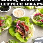 Overhead photo of Korean BBQ beef lettuce wraps arranged on a gray surface, filled with sliced marinated beef, kimchi, pickled onions, microgreens, and a dollop of red chili sauce, with small bowls of sesame seeds and black sesame in the background.