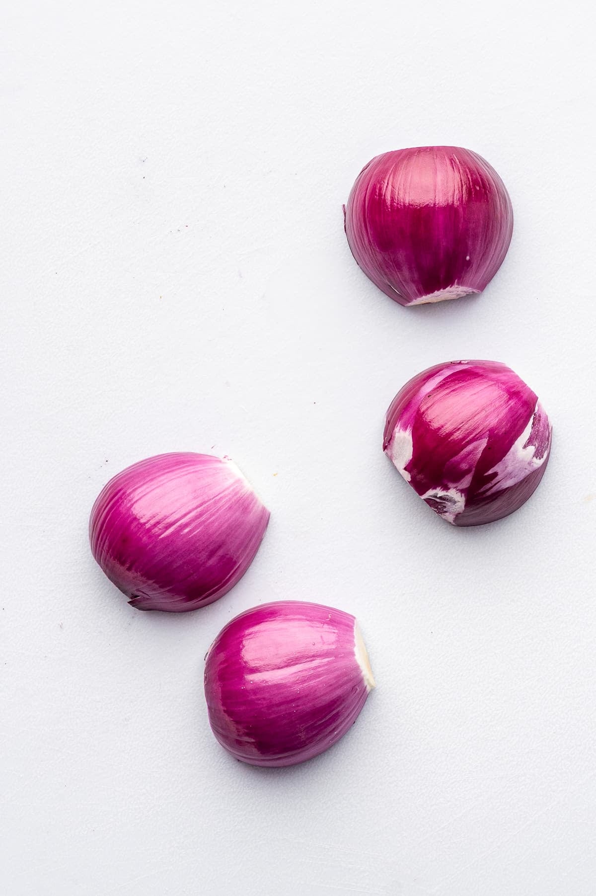 Four peeled pieces of red onion arranged on a white cutting board, showing glossy purple and magenta onion layers before being sliced for quick pickled red onions.