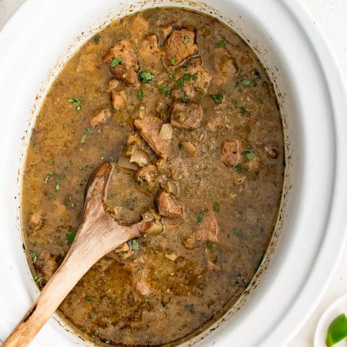 Fully cooked Crock Pot pork chile verde keeping warm in a large white slow cooker.