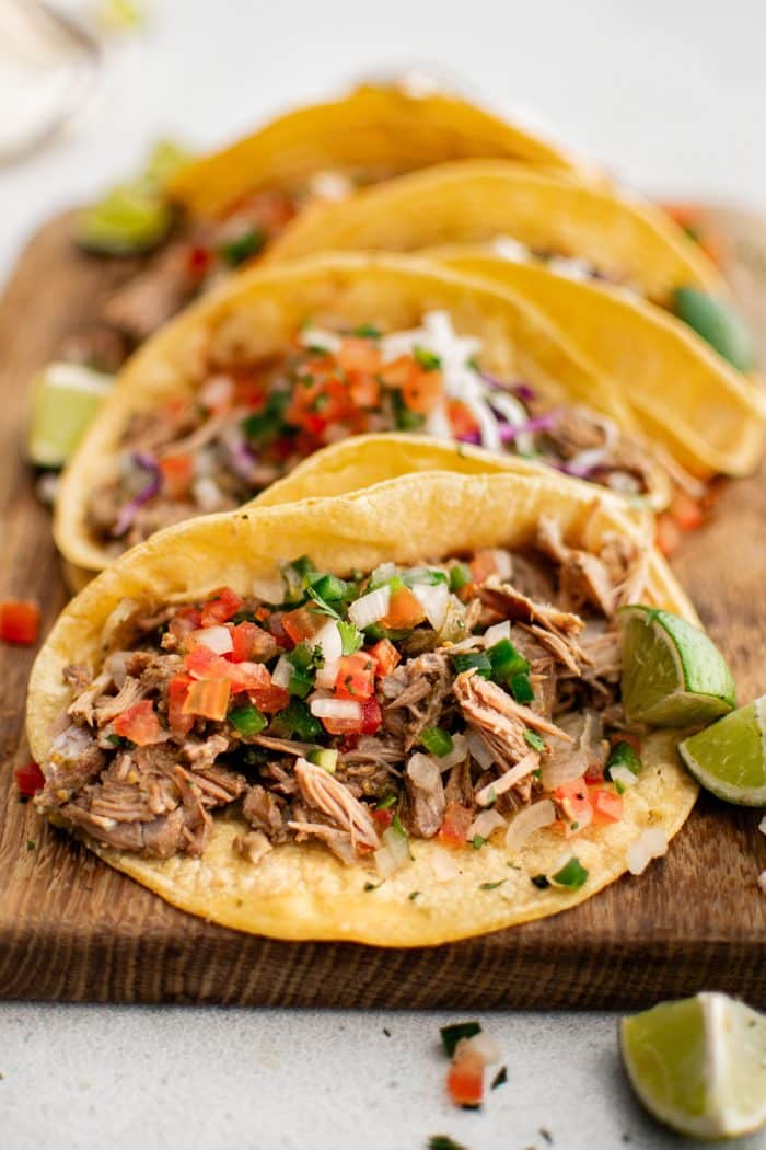 Corn tortillas filled with slow-cooked green chili pork, shredded red cabbage, and fresh pico de gallo with sliced limes on the side.