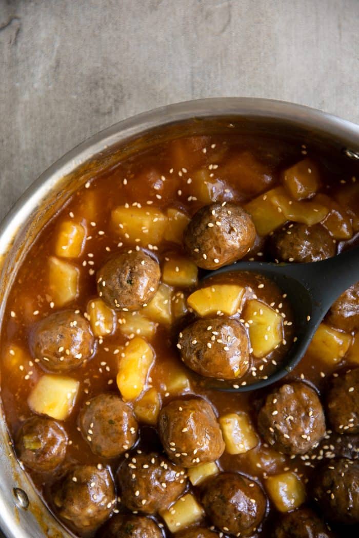 Shallow saucepan filled with homemade turkey meatballs simmering in a pineapple teriyaki sauce with pineapple.