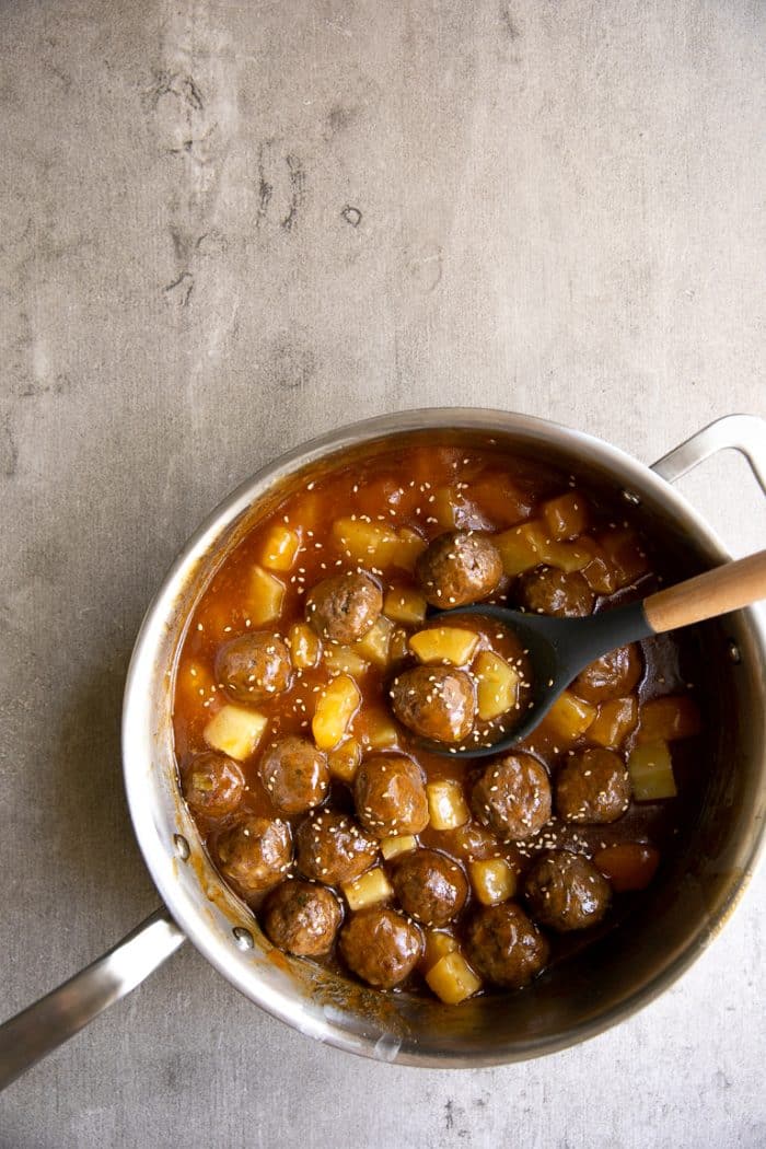 Shallow saucepan filled with homemade turkey meatballs simmering in a pineapple teriyaki sauce with pineapple.