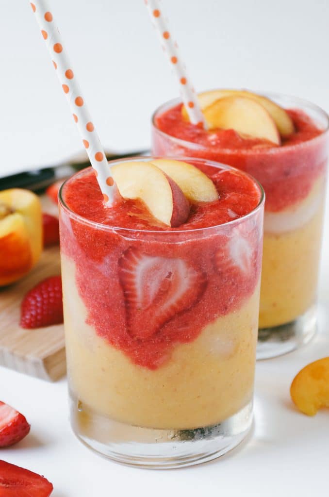 Layered strawberry peach smoothie with polka dot straw and fresh fruit